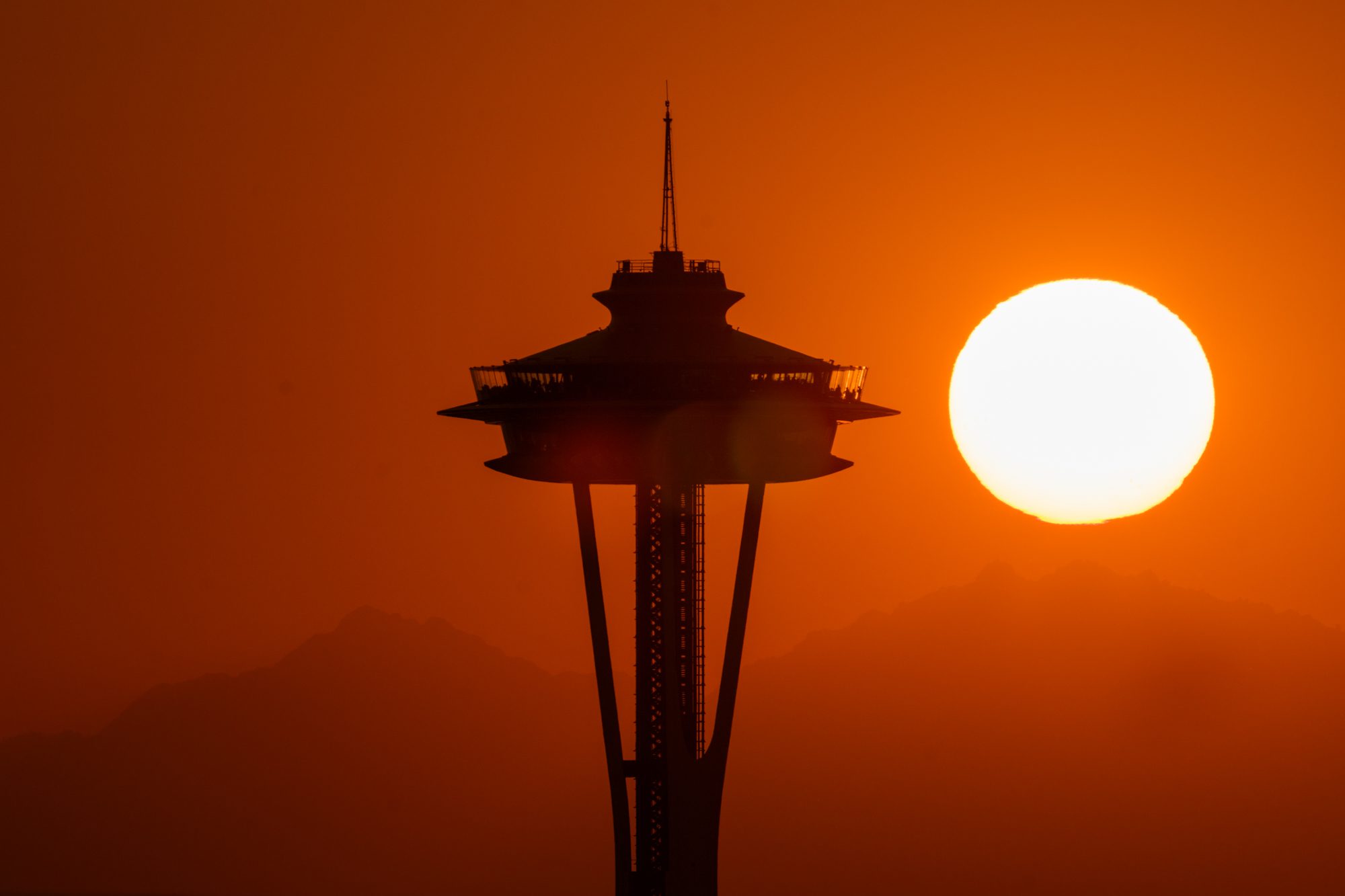 Image of full sun setting beside the Space Needle on a summer evening