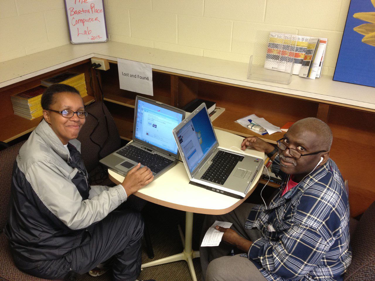 Two people sitting at a table with laptops looking at the camera smiling.