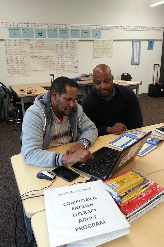 Two adult men work together together on a laptop in an adult computer literacy class