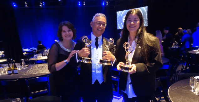 Two women and a man holding Emmy awards
