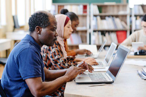 Three ethnically diverse individuals working on keyboards in a library